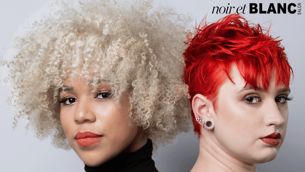 Two women with stylish, contrasting hairstyles at Noir et Blanc Salon: blonde curls and bright red pixie.