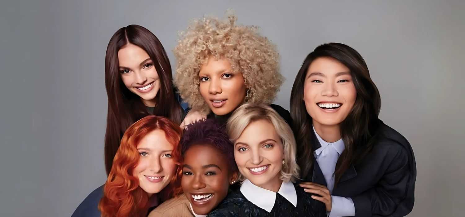 Group of six diverse, smiling women posing together against a neutral background.