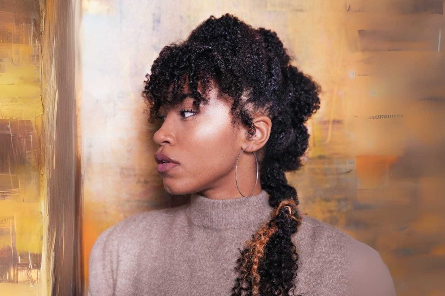 Woman with curly hair and braid, wearing hoop earring, against abstract background.