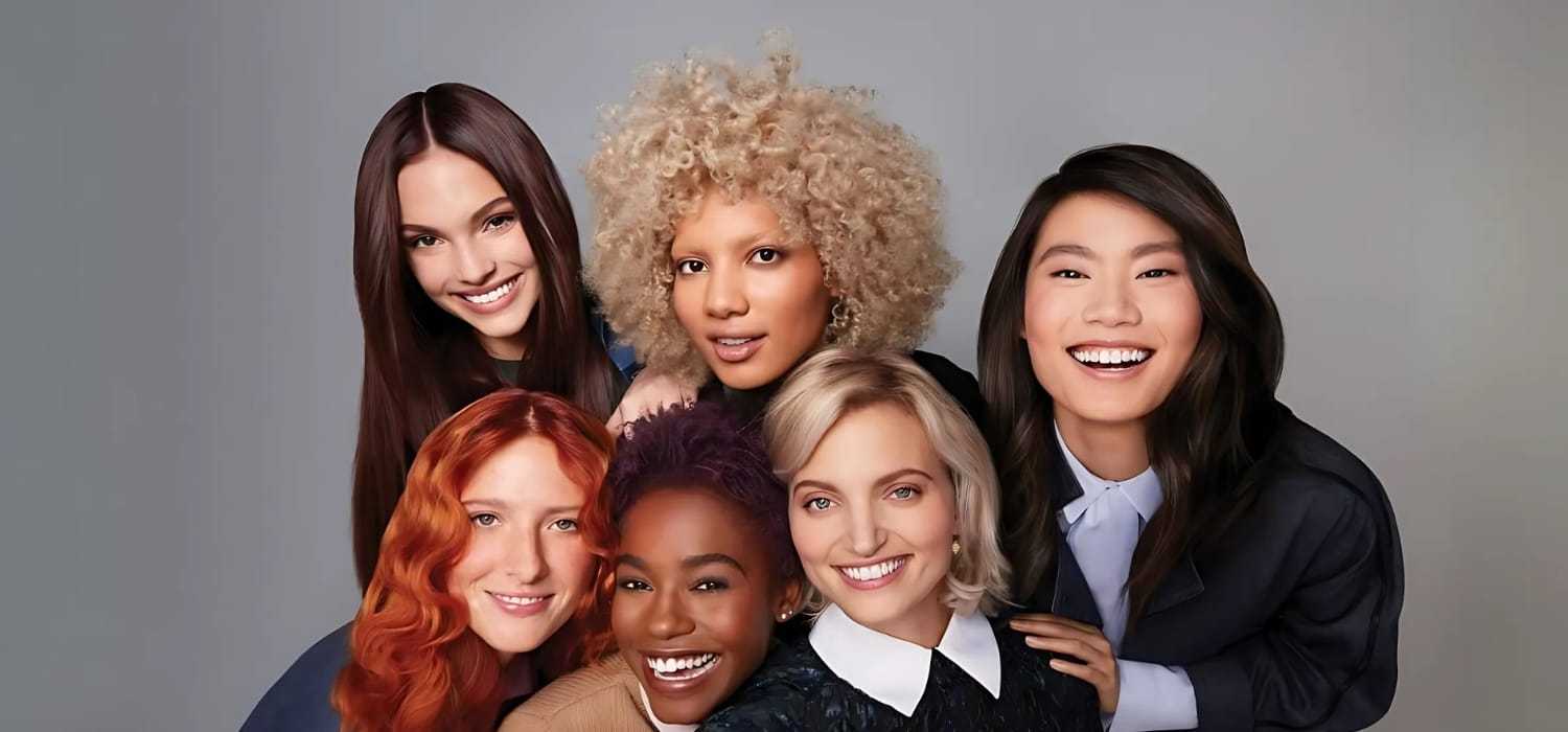 Group of six diverse, smiling women posing together against a neutral background.